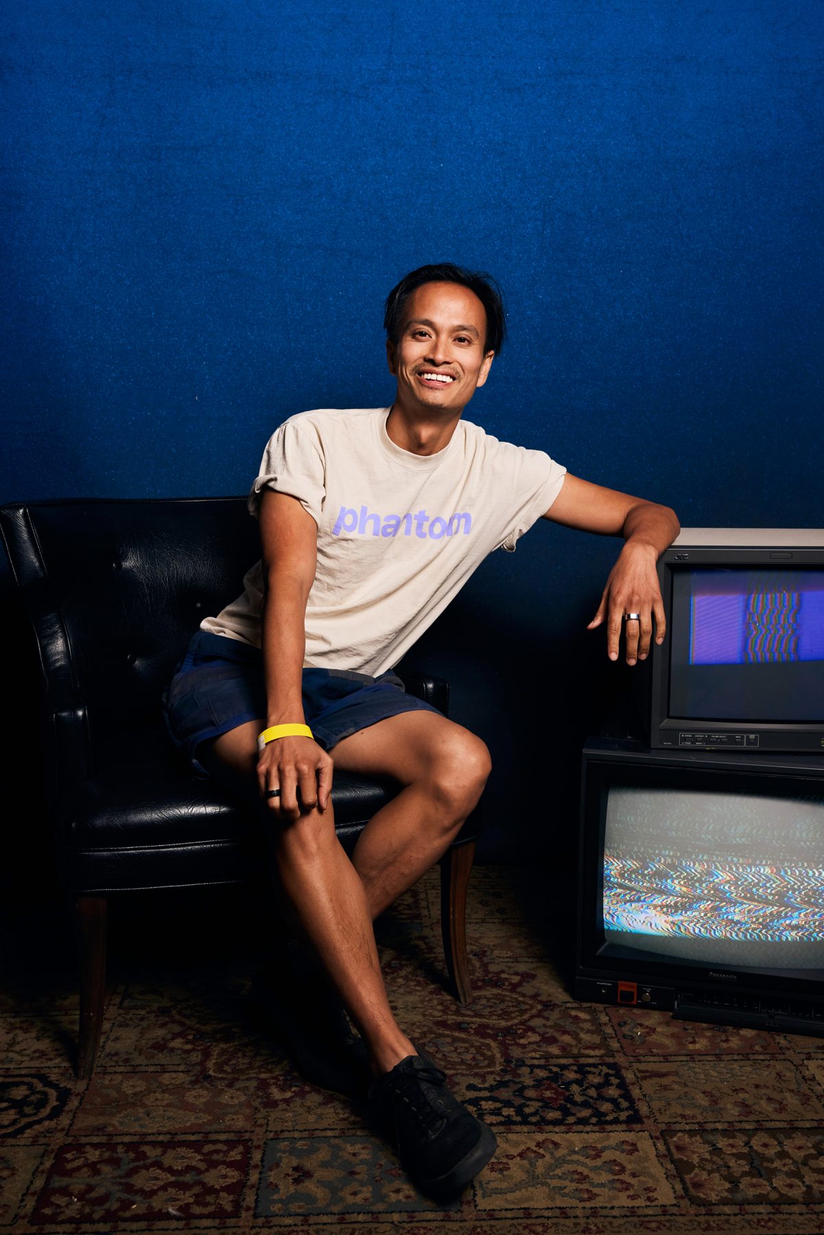 Phi sitting on a leather armchair in front of a deep blue wall and two old televisions