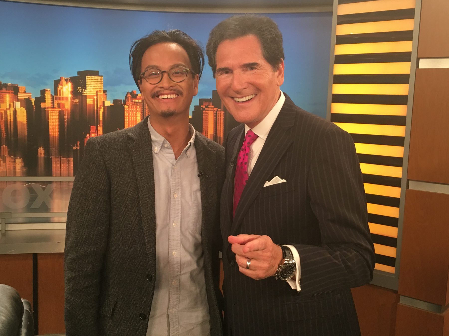 Phi standing with news anchor Ernie Anastos in a TV studio